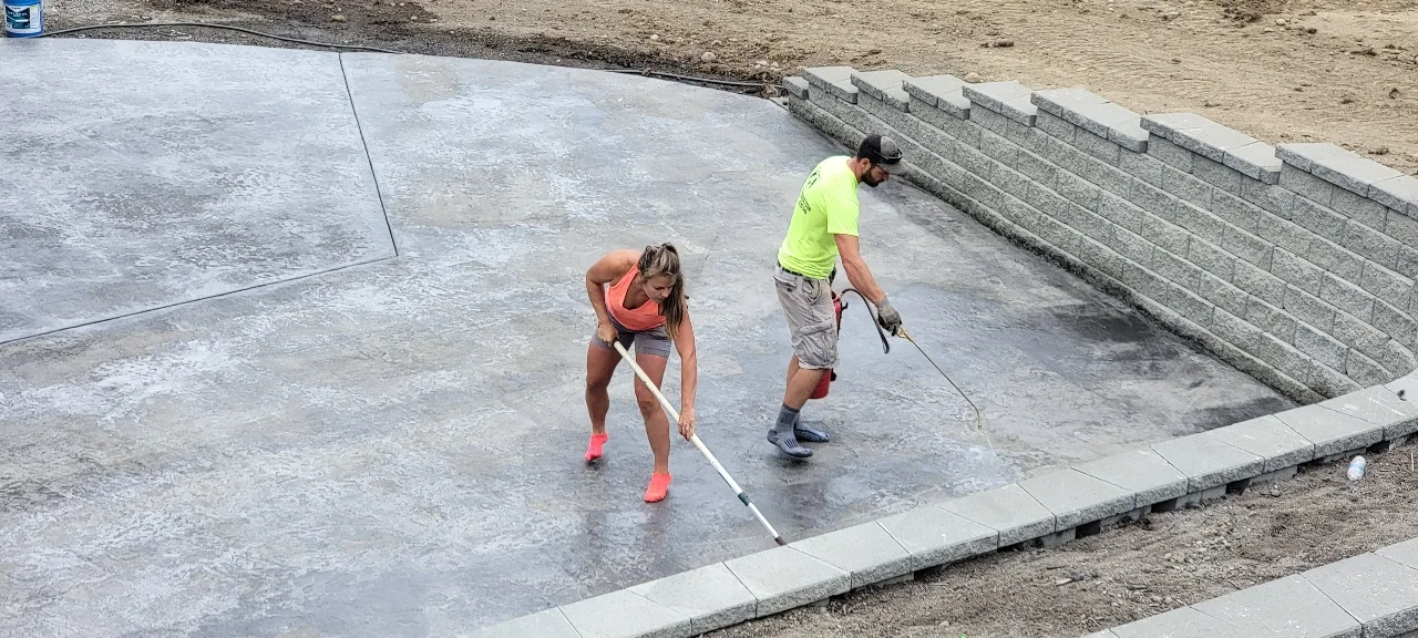 Grizzly crew finishing a large concrete patio beside a retaining wall